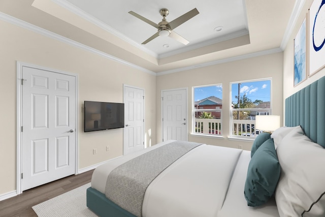 bedroom with dark wood-style floors, crown molding, a raised ceiling, and baseboards