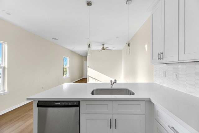 kitchen with a sink, backsplash, stainless steel dishwasher, a peninsula, and light countertops