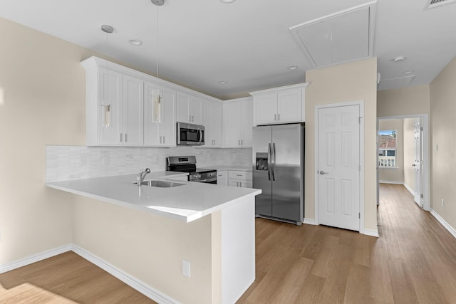 kitchen with wood finished floors, a peninsula, a sink, stainless steel appliances, and white cabinets