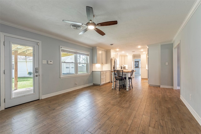 unfurnished dining area featuring wood finished floors, visible vents, baseboards, ceiling fan, and crown molding