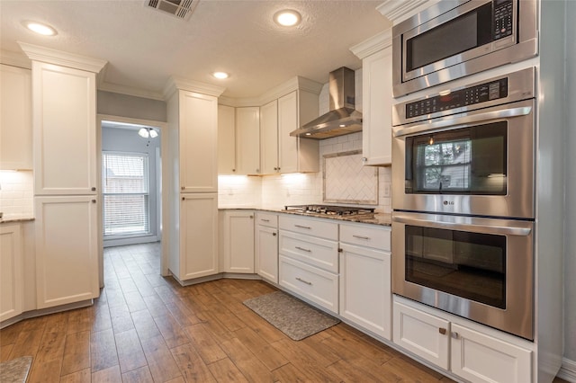 kitchen with tasteful backsplash, visible vents, light wood-type flooring, appliances with stainless steel finishes, and wall chimney exhaust hood