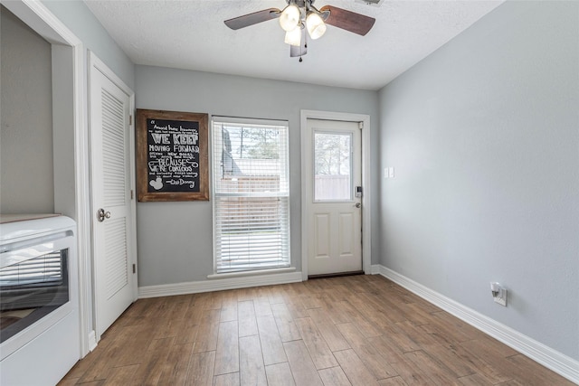 entryway with heating unit, wood finished floors, baseboards, ceiling fan, and a textured ceiling