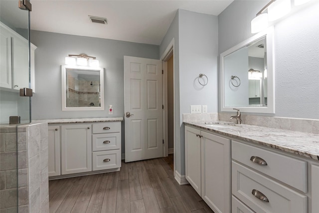 bathroom with visible vents, wood finished floors, vanity, and a tile shower