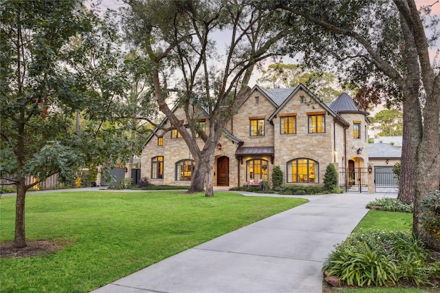 french provincial home with a gate, a standing seam roof, stone siding, a front yard, and metal roof