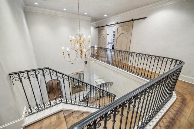 staircase with wood finished floors, a barn door, an inviting chandelier, crown molding, and baseboards