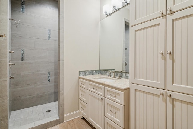 bathroom with vanity, wood finished floors, baseboards, and tiled shower