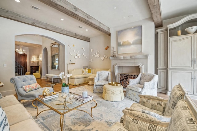 living area with visible vents, arched walkways, a lit fireplace, beamed ceiling, and a chandelier