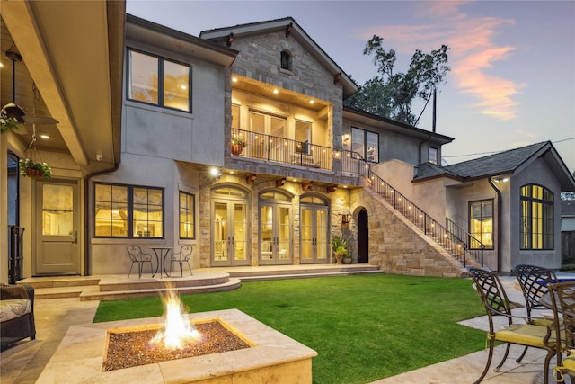 back of property featuring stone siding, a patio, french doors, a yard, and stairs