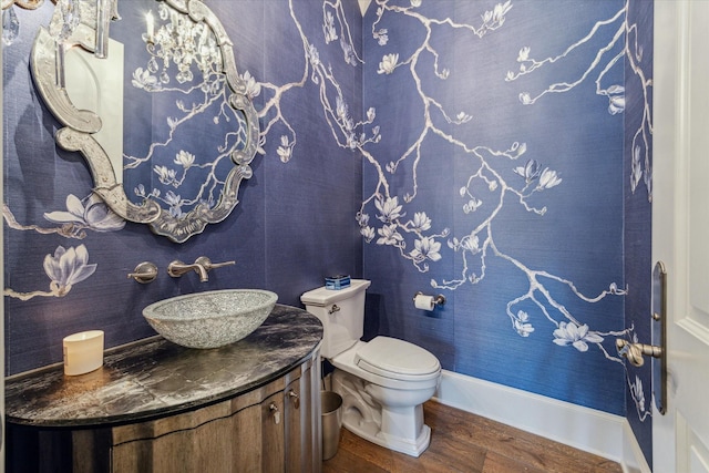 half bath featuring vanity, toilet, wood finished floors, and baseboards