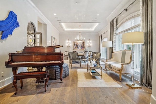 living area with hardwood / wood-style floors, an inviting chandelier, a raised ceiling, and ornamental molding