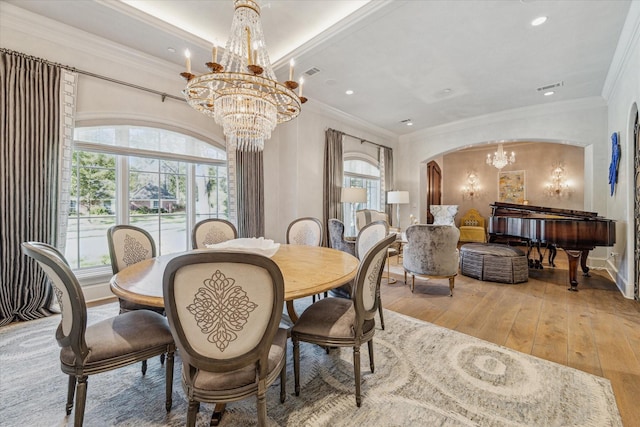 dining room featuring visible vents, a notable chandelier, hardwood / wood-style flooring, arched walkways, and crown molding