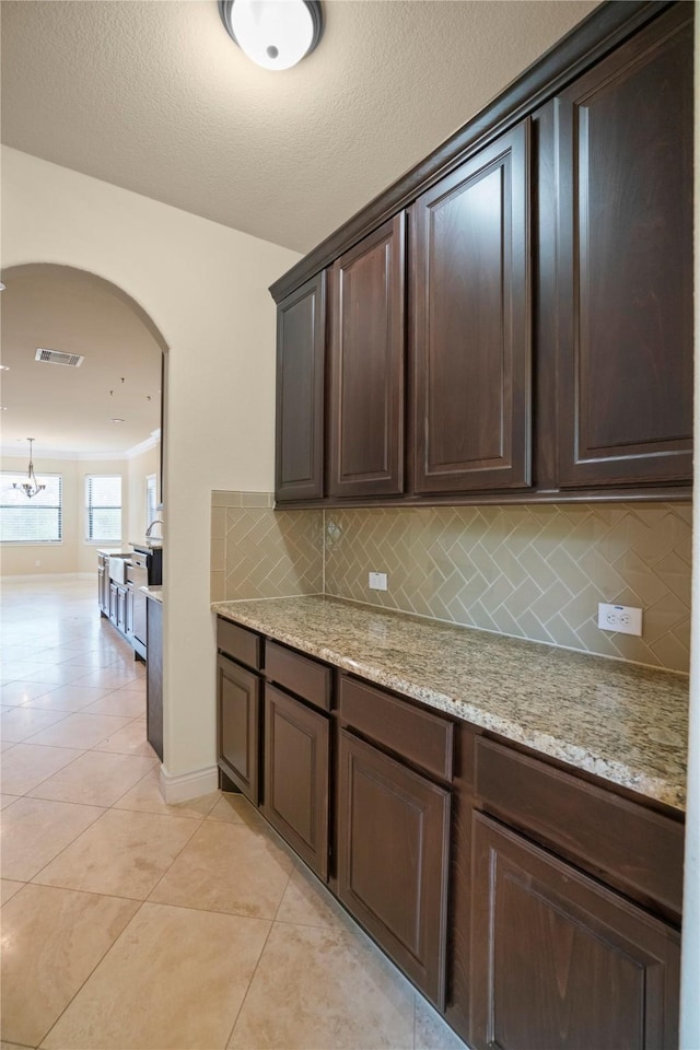 12530 Sharps Ln, Magnolia, TX 77354 - kitchen featuring dark brown cabinets, arched walkways, backsplash, light tile patterned floors, and light stone counters