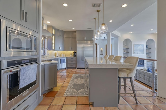 4206 Turks Pt, Galveston, TX 77554 - kitchen with visible vents, a kitchen island, a breakfast bar, gray cabinetry, and built in appliances