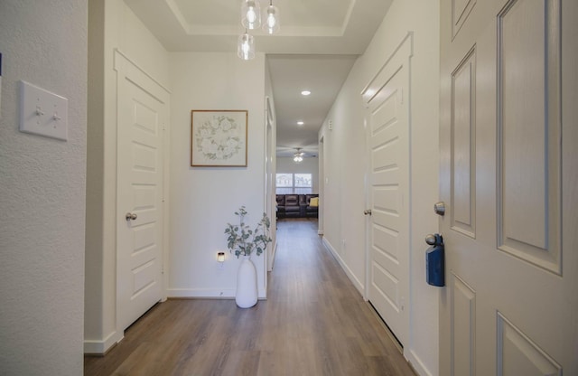 hallway with a tray ceiling, baseboards, and dark wood-style flooring