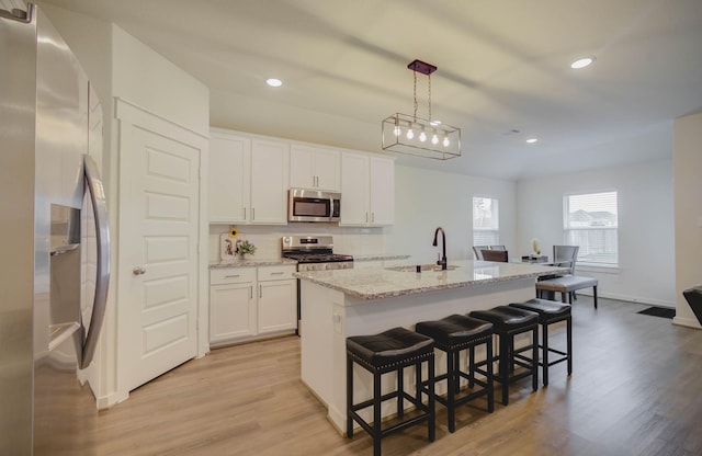 kitchen with an island with sink, a sink, appliances with stainless steel finishes, a kitchen bar, and light wood-type flooring