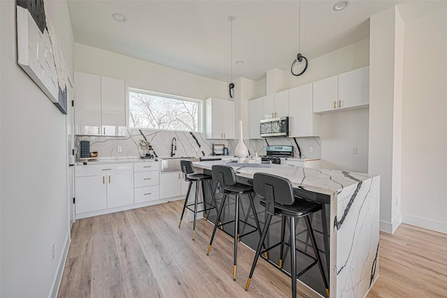 kitchen with a center island, light wood-type flooring, white cabinets, appliances with stainless steel finishes, and backsplash