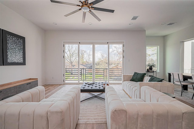 living room with light wood-style floors, baseboards, a ceiling fan, and visible vents