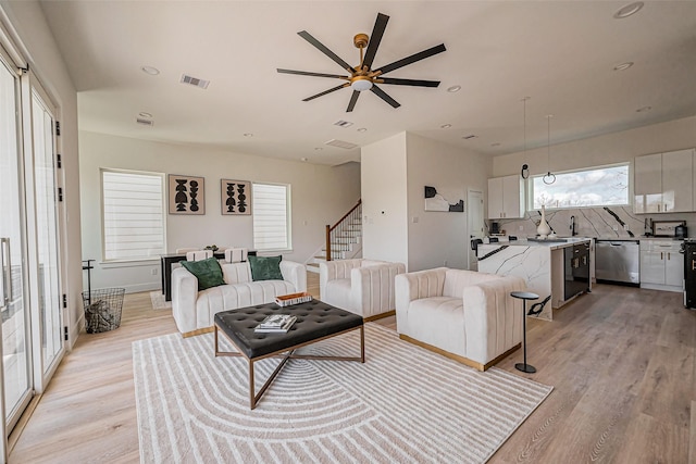 living area with light wood-style floors, a wealth of natural light, ceiling fan, and visible vents