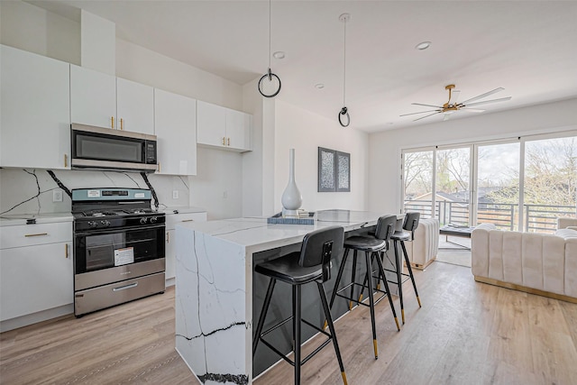 kitchen featuring light stone countertops, a center island, white cabinetry, light wood-style flooring, and stainless steel appliances