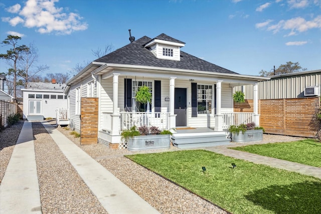 bungalow-style home with fence, covered porch, a shingled roof, an outdoor structure, and a front lawn