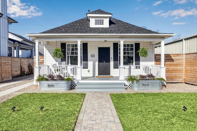 bungalow-style house featuring covered porch, a shingled roof, a front lawn, and fence