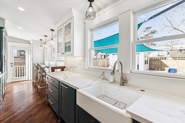 kitchen with a sink, glass insert cabinets, dark cabinets, dark wood-style flooring, and hanging light fixtures