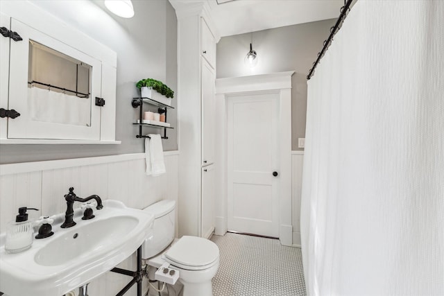 bathroom with a sink, tile patterned floors, toilet, and wainscoting