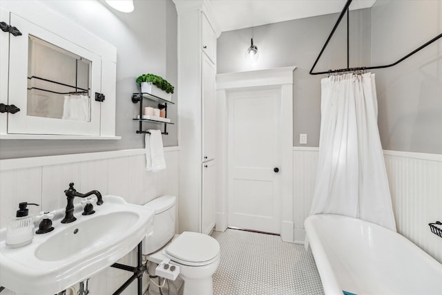 full bathroom with toilet, a tub to relax in, wainscoting, a shower with curtain, and a sink