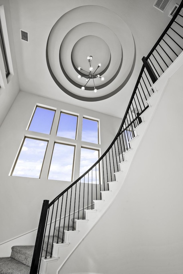 staircase with a raised ceiling, visible vents, a towering ceiling, and a chandelier