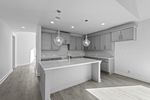 kitchen with gray cabinets, a sink, light wood-type flooring, a kitchen island with sink, and visible vents