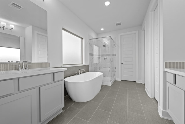 full bathroom with vanity, a freestanding tub, a marble finish shower, and visible vents