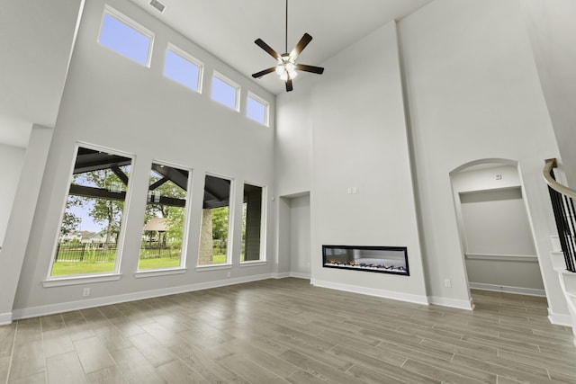 8407 Sheffields Leader, Fulshear, TX 77441 - unfurnished living room with a high ceiling, ceiling fan, stairway, wood finished floors, and a glass covered fireplace