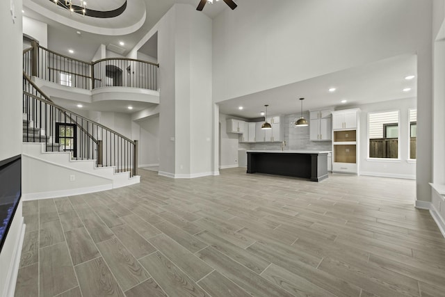 8407 Sheffields Leader, Fulshear, TX 77441 - unfurnished living room with light wood-style floors, a towering ceiling, ceiling fan, stairs, and recessed lighting