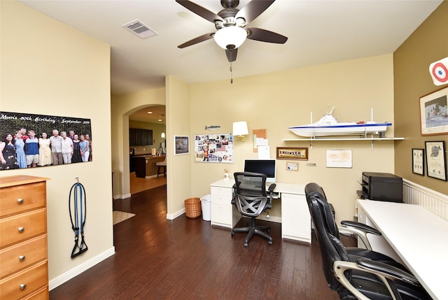 office featuring dark wood-style floors, baseboards, visible vents, arched walkways, and ceiling fan