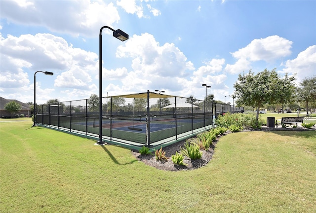 view of tennis court with a lawn and fence