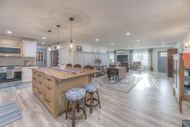 kitchen featuring a kitchen bar, wood counters, a kitchen island, stainless steel range with electric cooktop, and light wood finished floors