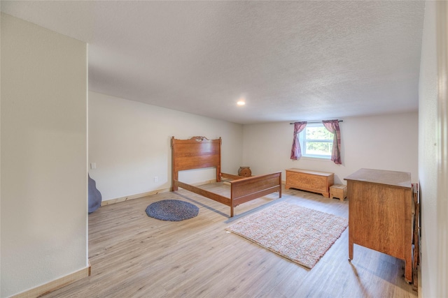 bedroom with a textured ceiling, baseboards, and wood finished floors