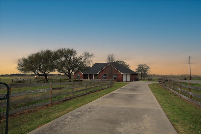 view of front facade with a front yard, concrete driveway, fence, and a rural view