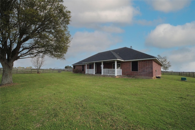back of property featuring covered porch, brick siding, fence, and a yard