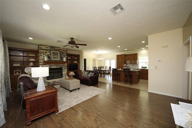 living room with a stone fireplace, ceiling fan, visible vents, and wood finished floors