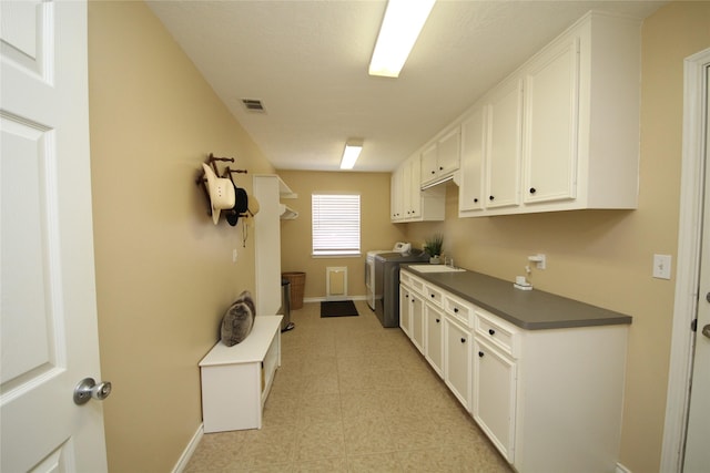 kitchen featuring white cabinetry, washer and clothes dryer, a sink, dark countertops, and visible vents