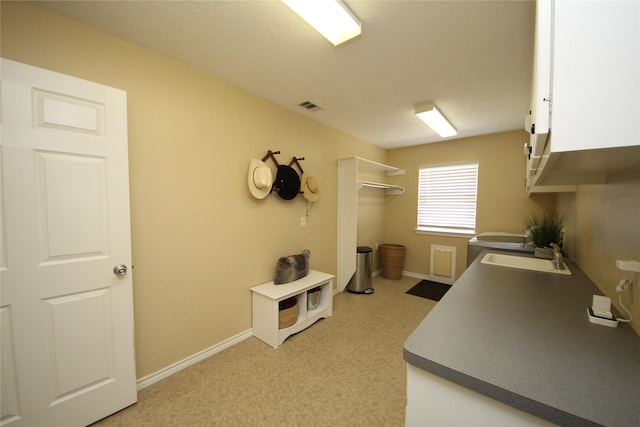 kitchen featuring baseboards, visible vents, light floors, and a sink