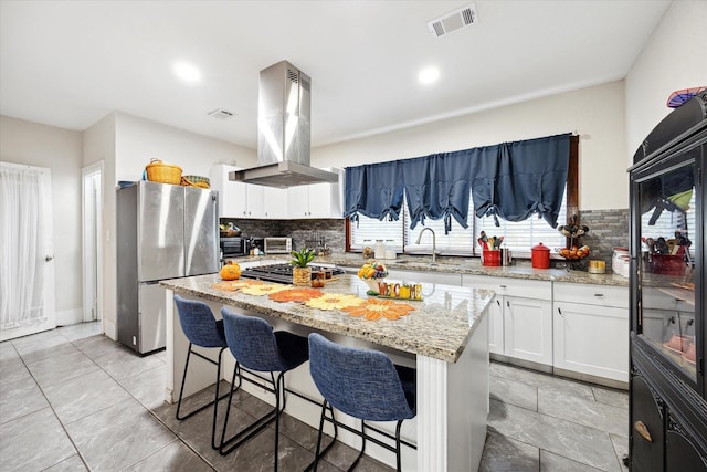725 Columbus Rd, Sealy, TX 77474 - kitchen featuring visible vents, island exhaust hood, a sink, freestanding refrigerator, and light stone countertops