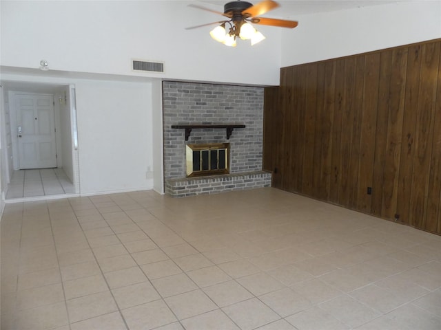 unfurnished living room with visible vents, wooden walls, a fireplace, light tile patterned floors, and ceiling fan