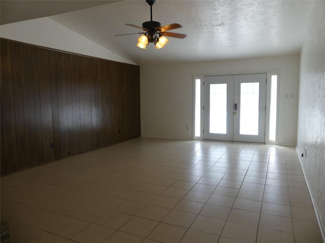 unfurnished room featuring french doors, wooden walls, light tile patterned floors, ceiling fan, and vaulted ceiling