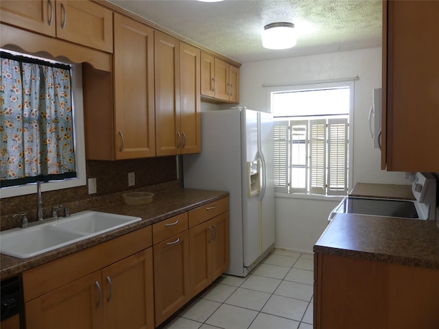 kitchen featuring light tile patterned floors, white appliances, dark countertops, and a sink