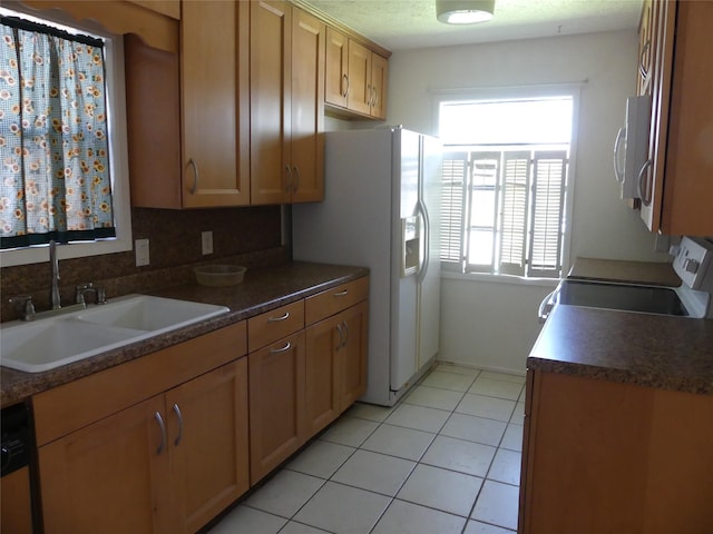 kitchen with a sink, backsplash, dark countertops, white appliances, and light tile patterned floors