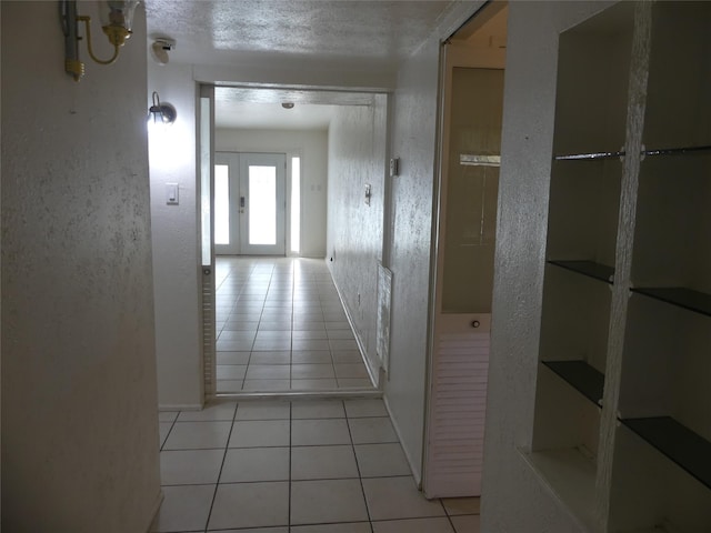 hall featuring light tile patterned flooring, a textured wall, and a textured ceiling