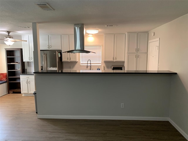 kitchen featuring visible vents, dark countertops, white cabinetry, freestanding refrigerator, and island range hood