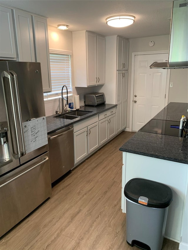 kitchen featuring light wood-style flooring, a sink, dark stone countertops, stainless steel appliances, and exhaust hood